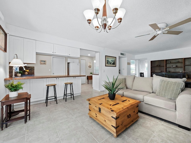 tiled living room with ceiling fan with notable chandelier and a textured ceiling