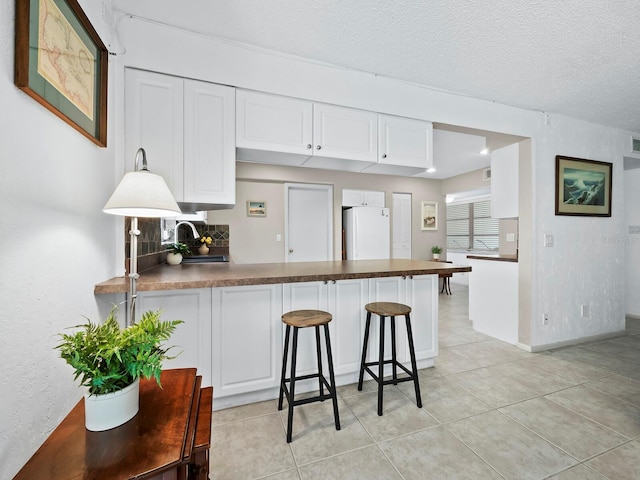 kitchen with white cabinets, white refrigerator, kitchen peninsula, a breakfast bar area, and a textured ceiling