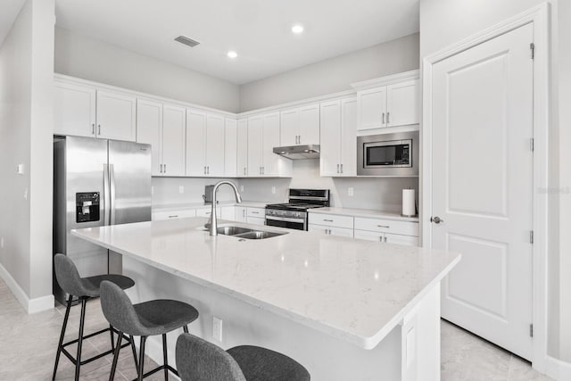 kitchen with stainless steel appliances, light stone counters, sink, white cabinetry, and a kitchen island with sink