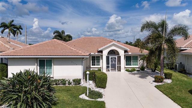 view of front of home with central AC unit, concrete driveway, a tiled roof, stucco siding, and a front yard