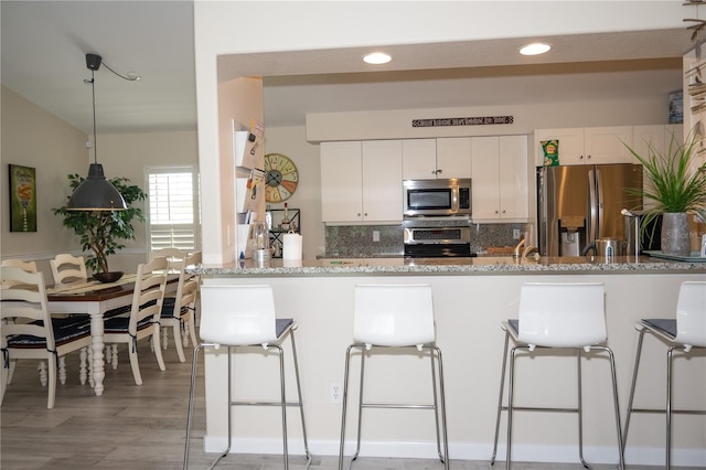 kitchen featuring a peninsula, light stone countertops, stainless steel appliances, a kitchen bar, and white cabinetry