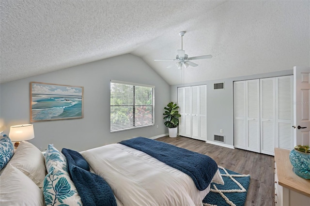 bedroom with dark wood-type flooring, multiple closets, a textured ceiling, ceiling fan, and lofted ceiling