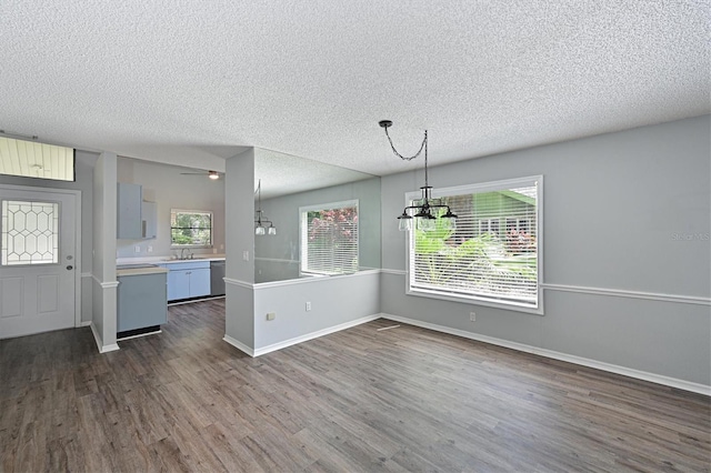 unfurnished dining area with sink, dark wood-type flooring, a textured ceiling, and a chandelier