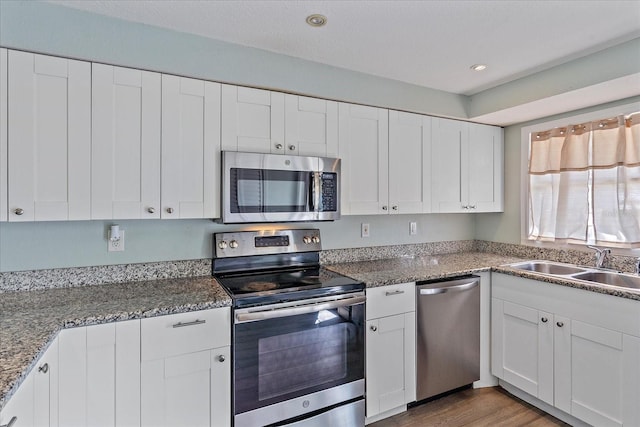 kitchen with light wood-type flooring, appliances with stainless steel finishes, white cabinets, dark stone counters, and sink