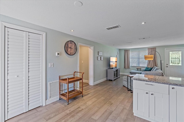 kitchen with a textured ceiling, white cabinetry, stone countertops, and light hardwood / wood-style floors