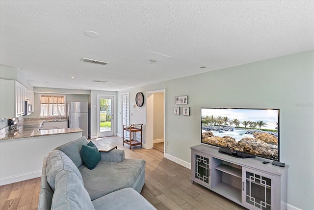 living room featuring sink, a textured ceiling, and light hardwood / wood-style floors