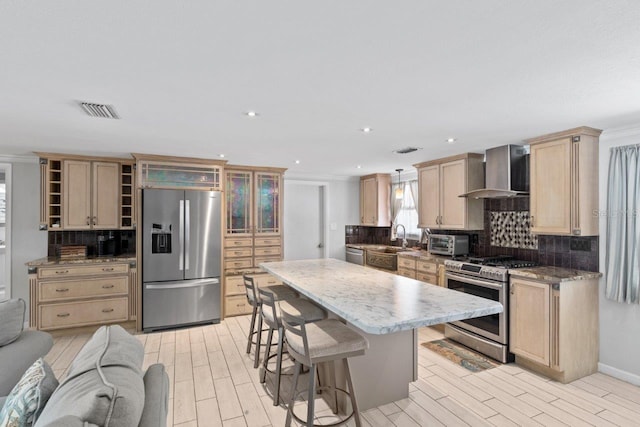 kitchen with sink, wall chimney range hood, a kitchen breakfast bar, a kitchen island, and appliances with stainless steel finishes