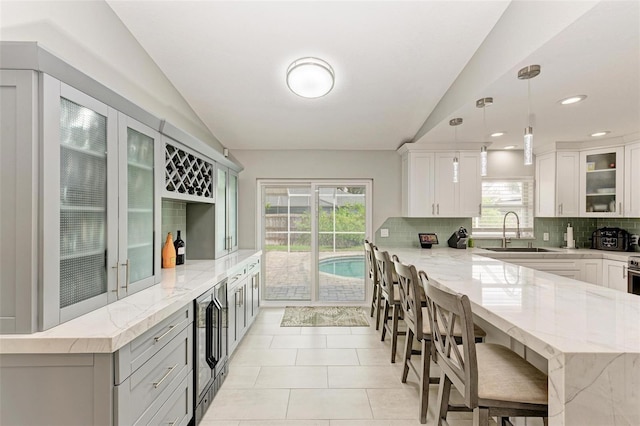 kitchen with light stone countertops, decorative light fixtures, lofted ceiling, and sink