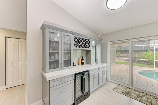 bar with gray cabinets, light stone counters, wine cooler, and lofted ceiling