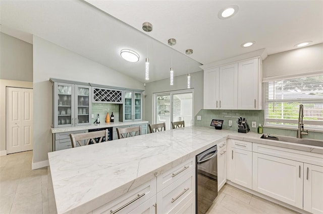 kitchen with sink, kitchen peninsula, lofted ceiling, decorative light fixtures, and white cabinets