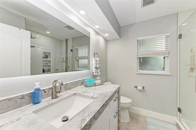 bathroom featuring tile patterned flooring, vanity, a shower with shower door, and toilet