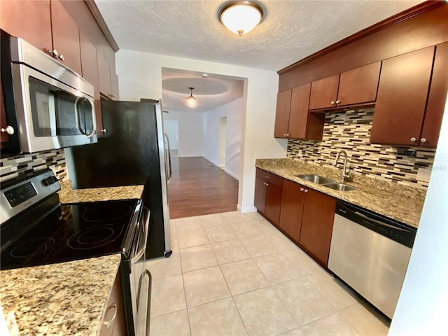 kitchen featuring sink, light tile patterned floors, appliances with stainless steel finishes, backsplash, and a textured ceiling