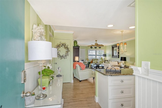 kitchen featuring ceiling fan with notable chandelier, light hardwood / wood-style floors, kitchen peninsula, ornamental molding, and white cabinets