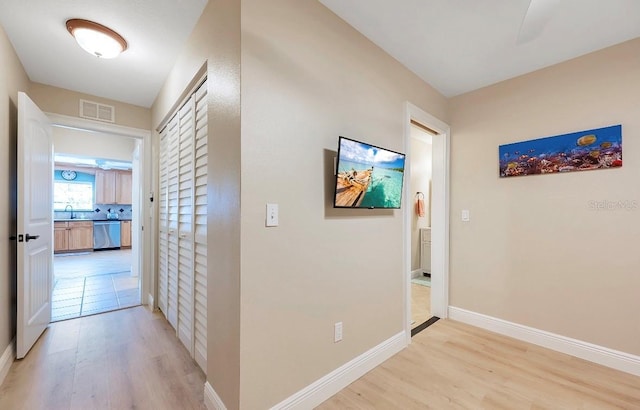 corridor with baseboards, light wood-style flooring, visible vents, and a sink