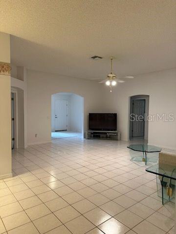 unfurnished living room with ceiling fan, a textured ceiling, and light tile patterned floors