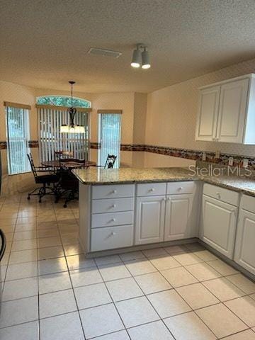 kitchen with a textured ceiling, light stone counters, light tile patterned flooring, and white cabinets