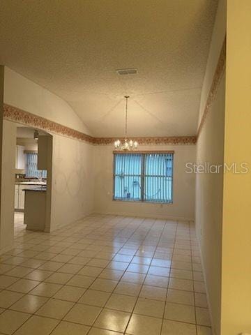 empty room featuring light tile patterned flooring, lofted ceiling, a textured ceiling, and a chandelier