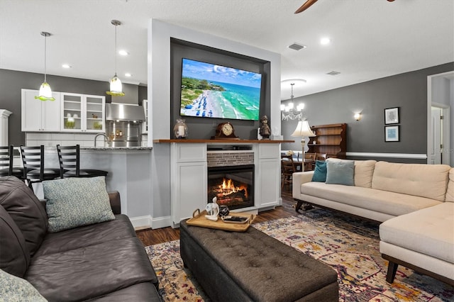 living room featuring recessed lighting, visible vents, dark wood-type flooring, a glass covered fireplace, and ceiling fan with notable chandelier