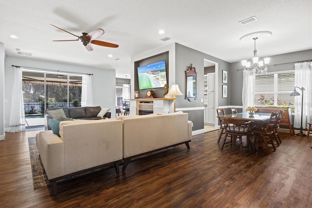 living area with visible vents, dark wood finished floors, a textured ceiling, a fireplace, and ceiling fan with notable chandelier