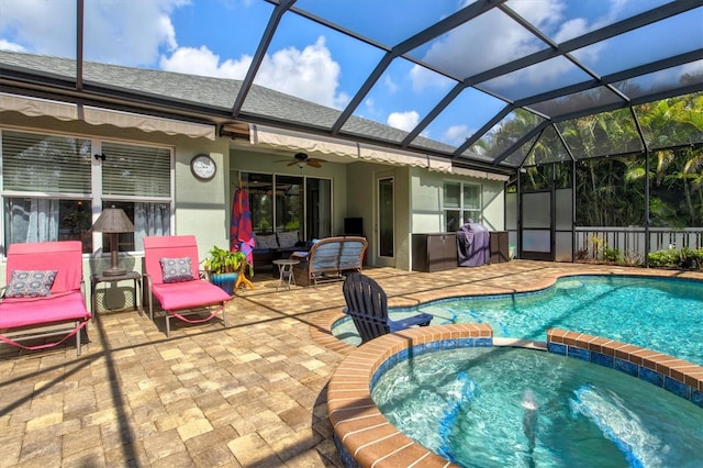 view of pool featuring a pool with connected hot tub, grilling area, a ceiling fan, a patio area, and glass enclosure