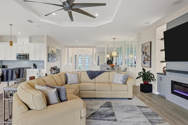 living room featuring a tray ceiling, french doors, ceiling fan, and light hardwood / wood-style floors