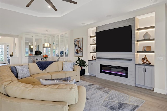 living room with light wood-type flooring, ceiling fan, and a raised ceiling