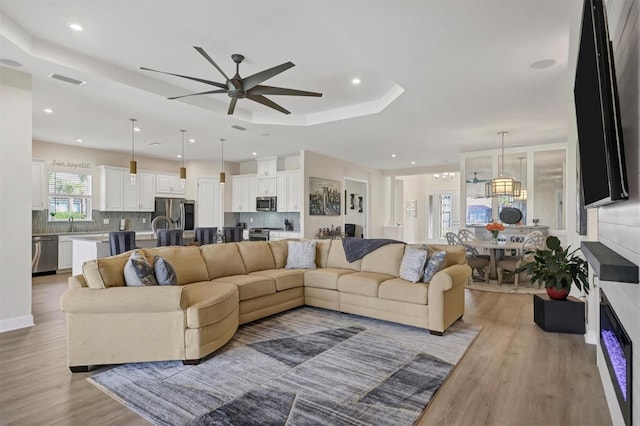 living room with sink, a raised ceiling, ceiling fan, and light hardwood / wood-style flooring