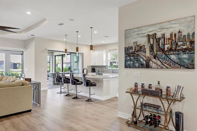 kitchen with light wood-type flooring, decorative light fixtures, light stone counters, white cabinets, and a breakfast bar area