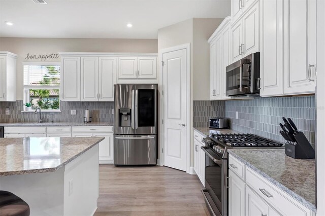 kitchen with white cabinets, stainless steel appliances, light stone countertops, and tasteful backsplash