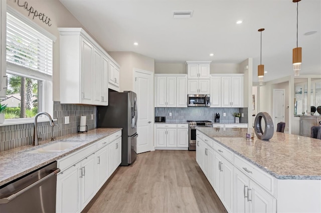 kitchen featuring white cabinetry, hanging light fixtures, a center island, sink, and appliances with stainless steel finishes