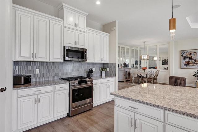 kitchen featuring white cabinetry, backsplash, appliances with stainless steel finishes, and decorative light fixtures