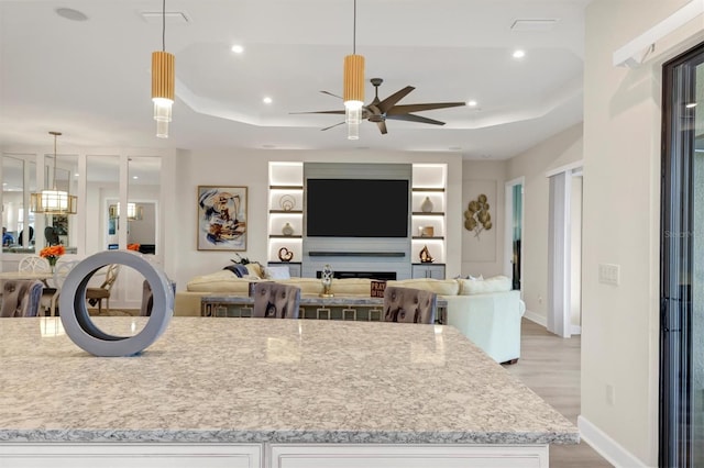 kitchen with a tray ceiling, pendant lighting, white cabinetry, and light stone countertops