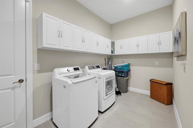 clothes washing area with cabinets, light tile patterned flooring, and washing machine and clothes dryer