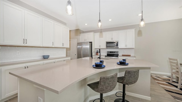 kitchen with white cabinets, decorative light fixtures, stainless steel appliances, and an island with sink