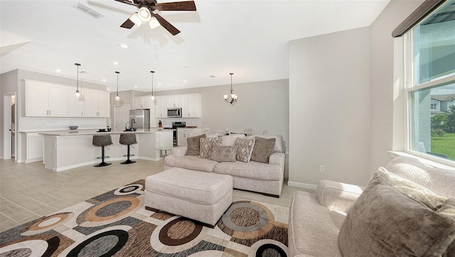 tiled living room with ceiling fan with notable chandelier and sink