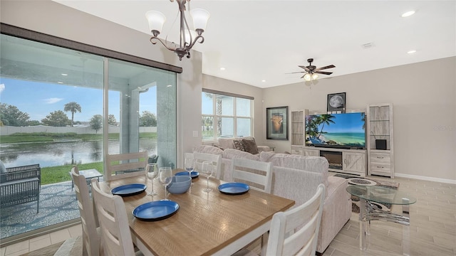 dining room featuring ceiling fan with notable chandelier and a water view