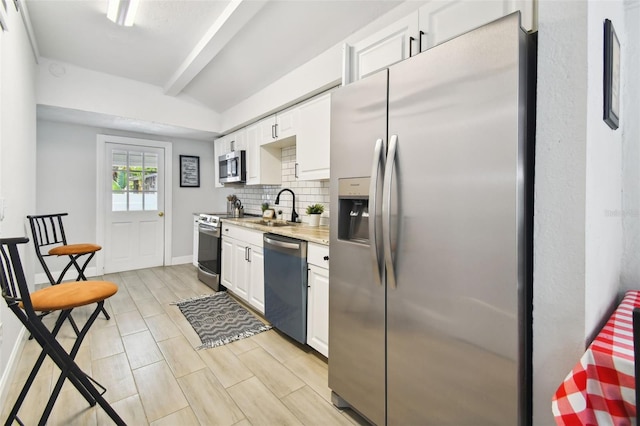 kitchen with stainless steel appliances, white cabinets, backsplash, sink, and beamed ceiling