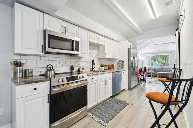 kitchen with stainless steel appliances, sink, backsplash, white cabinetry, and vaulted ceiling with beams