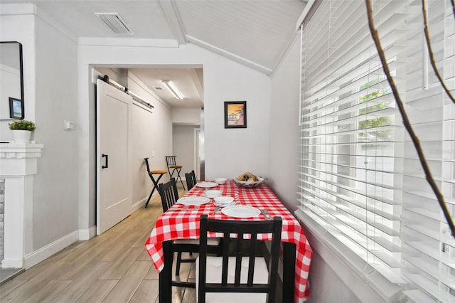 dining area with a barn door, light wood-type flooring, and vaulted ceiling