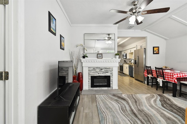 living room with ceiling fan, light wood-type flooring, a fireplace, and vaulted ceiling