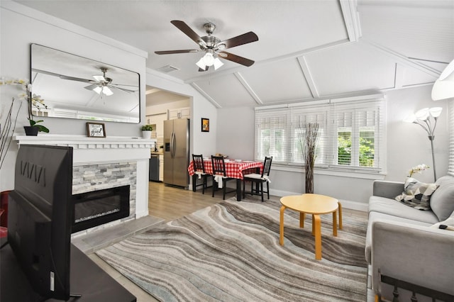 living room with ceiling fan, a stone fireplace, vaulted ceiling, and light hardwood / wood-style floors