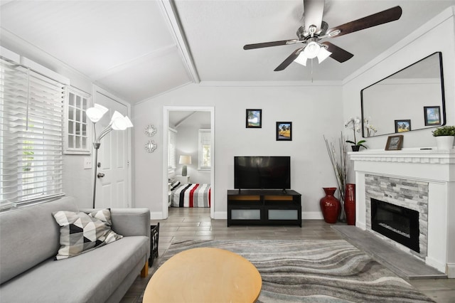 living room with ceiling fan, hardwood / wood-style flooring, a stone fireplace, and vaulted ceiling