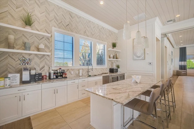 kitchen with light stone countertops, a kitchen island, decorative light fixtures, a breakfast bar, and white cabinets