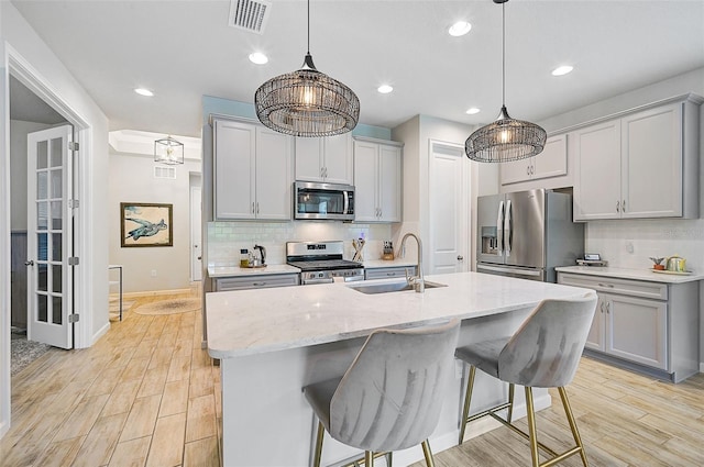 kitchen featuring sink, an island with sink, light hardwood / wood-style floors, decorative backsplash, and appliances with stainless steel finishes