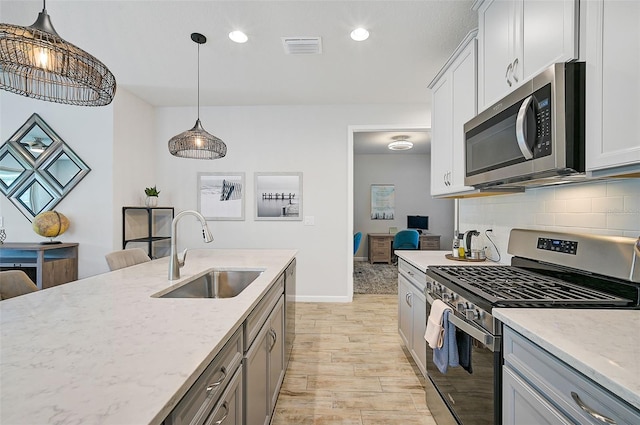 kitchen featuring pendant lighting, sink, light hardwood / wood-style flooring, light stone countertops, and appliances with stainless steel finishes