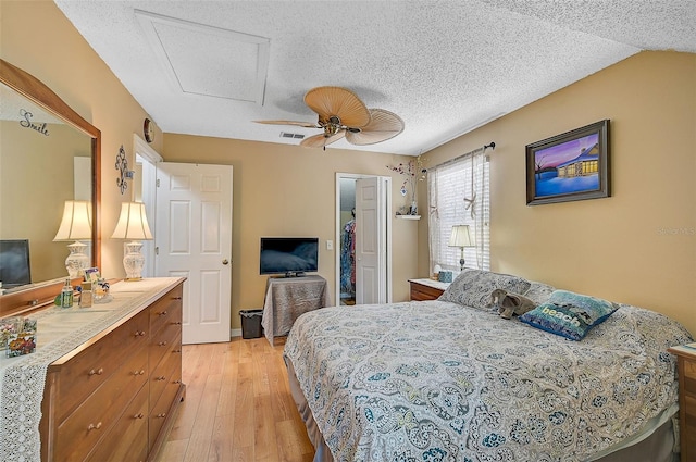 bedroom with a textured ceiling, ceiling fan, a spacious closet, light hardwood / wood-style flooring, and lofted ceiling