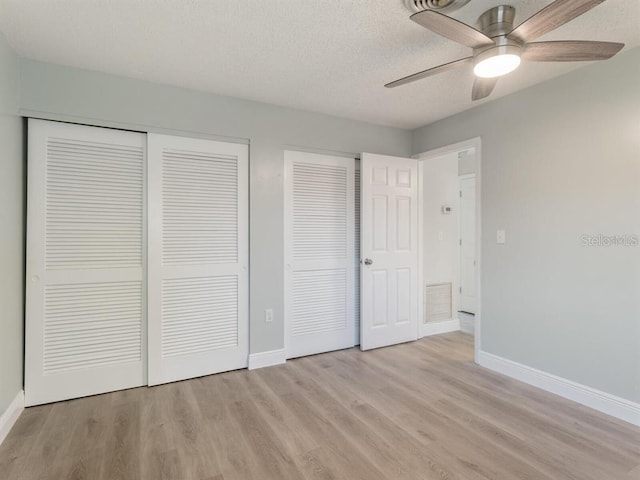 unfurnished bedroom with a textured ceiling, two closets, ceiling fan, and light hardwood / wood-style floors