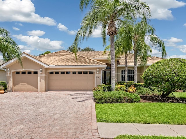 view of front facade featuring a garage, a tile roof, decorative driveway, and stucco siding