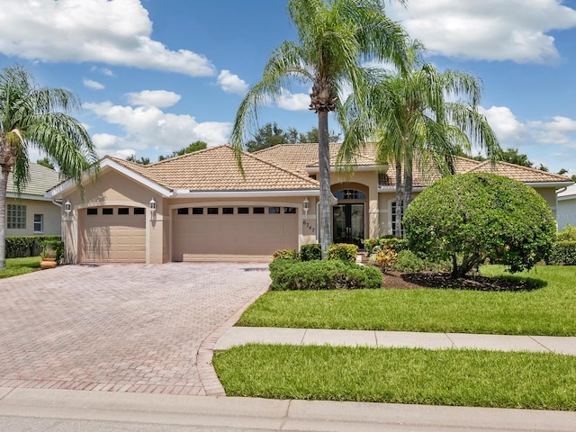 mediterranean / spanish-style house with an attached garage, a tiled roof, decorative driveway, stucco siding, and a front lawn