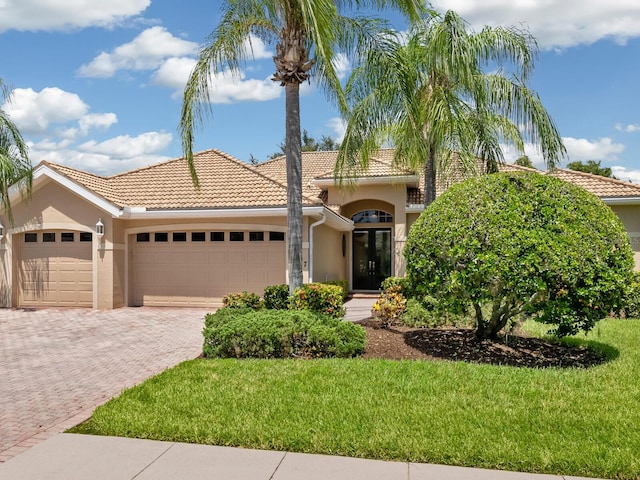 mediterranean / spanish house with a garage, a tiled roof, decorative driveway, a front lawn, and stucco siding